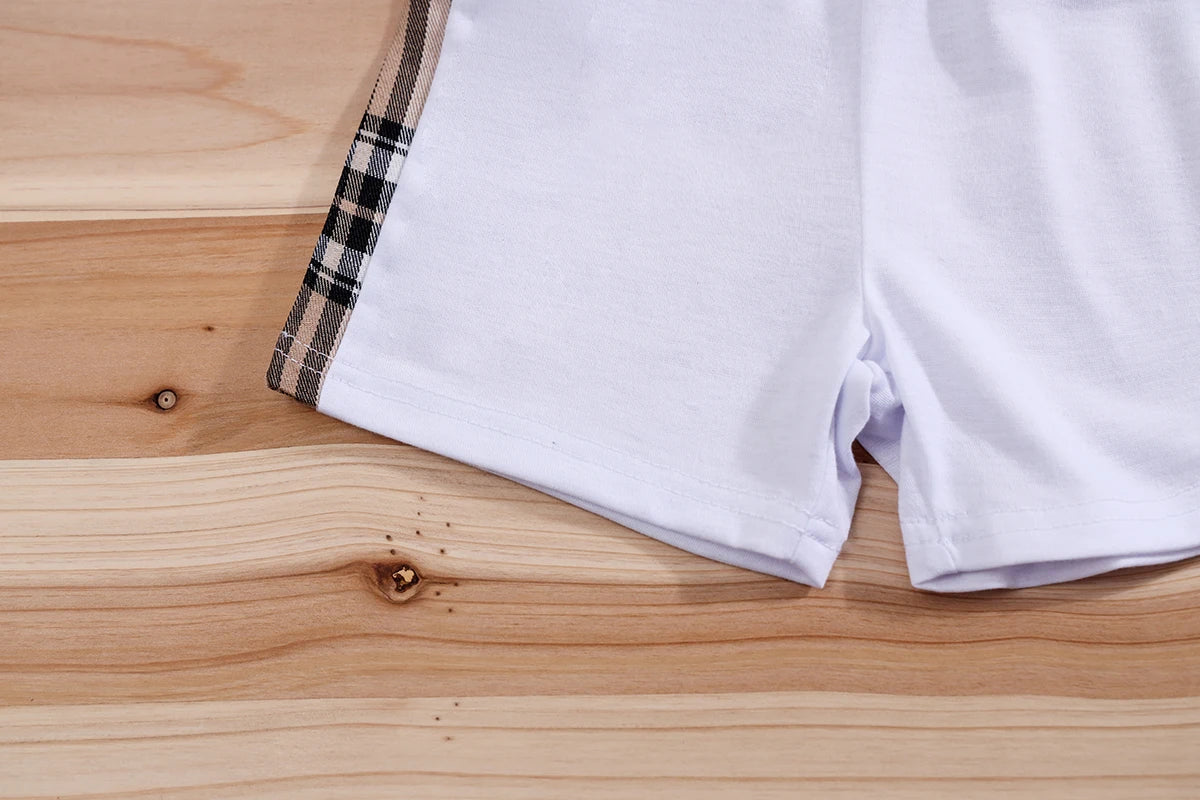Conjunto roupa infantil menino estampa divertida IURNXB shorts brancos com faixa xadrez lateral sobre mesa de madeira