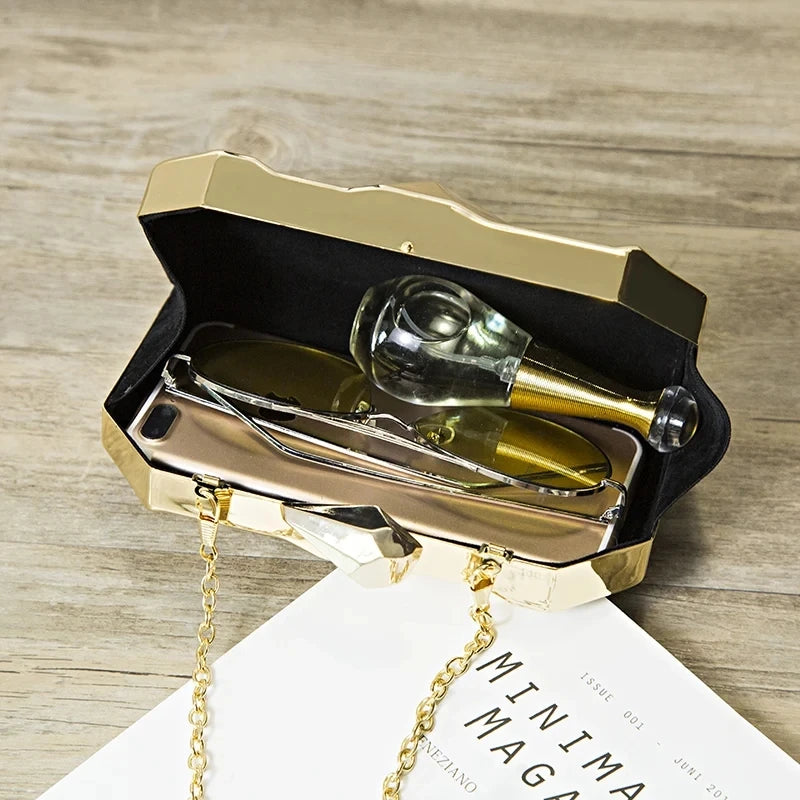 Bolsa dourada elegante aberta mostrando acessórios como óculos e um perfume dentro