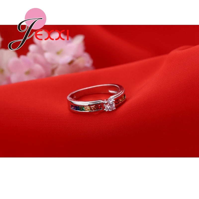 Anel de compromisso JEXXI com design elegante e pedra central brilhante em fundo vermelho