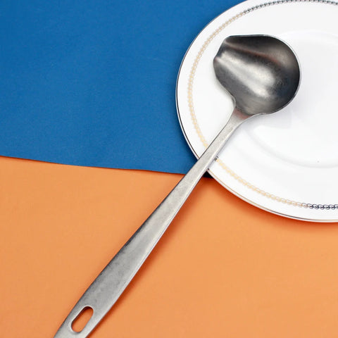 Colher concha escumadeira de inox LUCF com cabo ergonômico sobre prato branco e fundo colorido