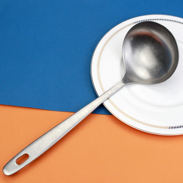 Colher concha escumadeira de aço inoxidável sobre prato branco em fundo colorido