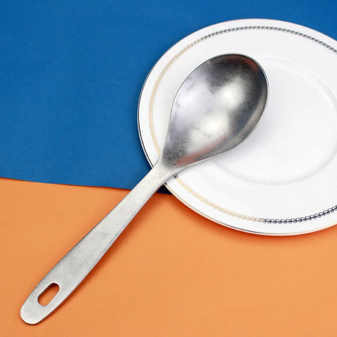 Colher concha escumadeira de aço inoxidável sobre prato branco em fundo azul e laranja