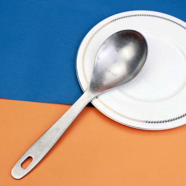 Colher concha escumadeira de aço inoxidável sobre prato branco em fundo azul e laranja