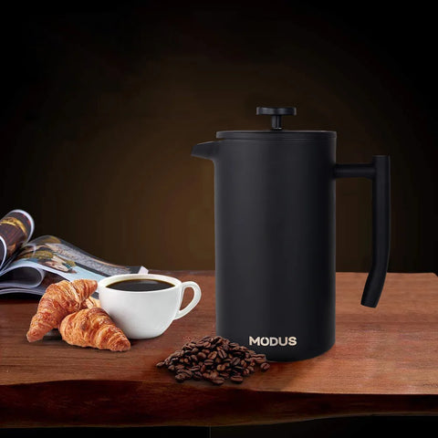 Cafeteira prensa francesa inox MODUS com café fresco, croissant e grãos de café ao fundo